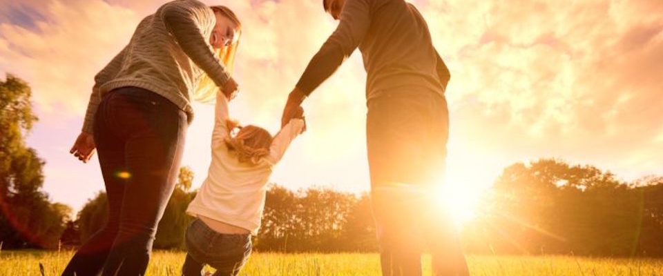 Happy family in the park evening light. The lights of a sun. Mom, dad and baby happy walk at sunset. The concept of a happy family.Parents hold the baby’s hands.