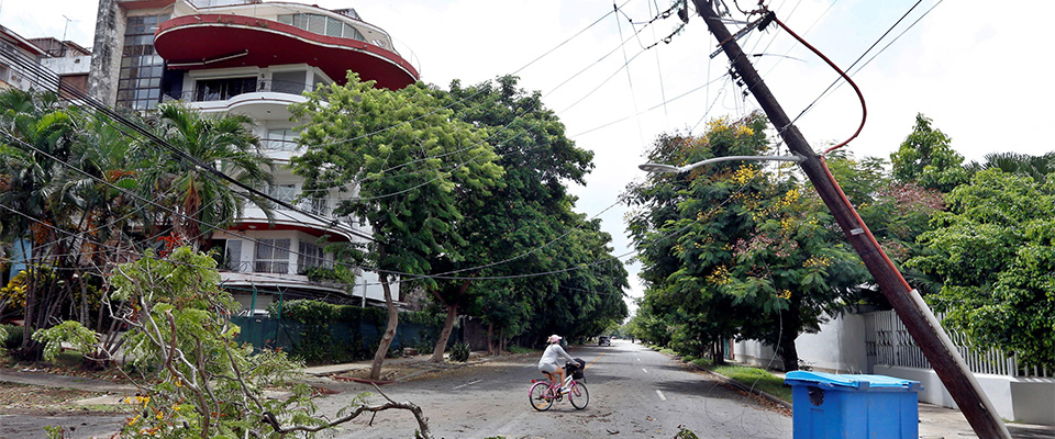 epa08625451 A woman on a bicycle passes next to the branches of a fallen tree and a crooked electric pole after the passage of Tropical Storm Laura, in Havana, Cuba, 25 August 2020. Cuba began on 25 August throughout its territory the recovery and evaluation phase of the damage caused by tropical storm Laura, which between 23 and 24 August traveled the island from end to end without leaving victims but damaging the electrical networks, homes and crops.  EPA/Ernesto Mastrascusa